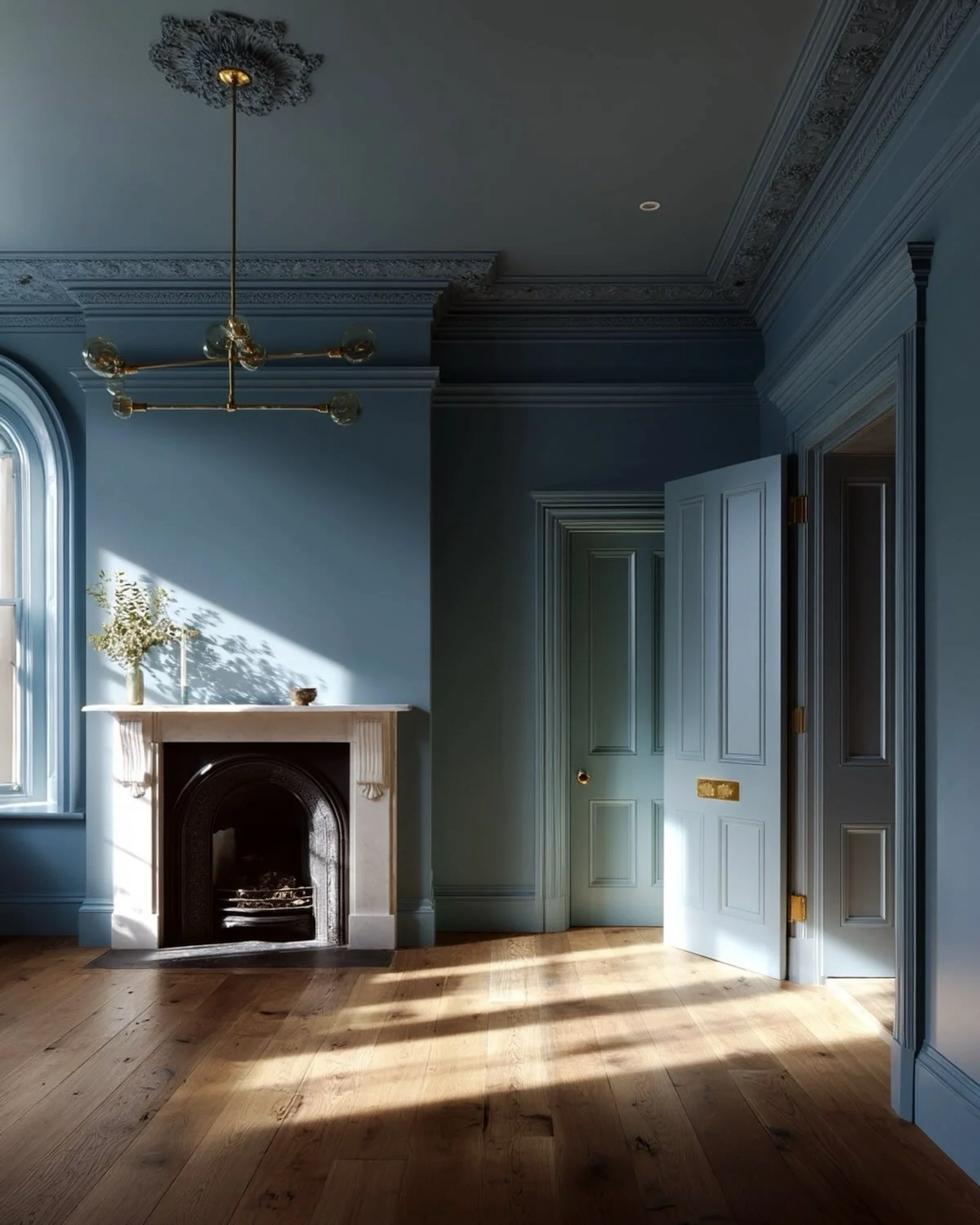 Blue painted period room with ornate cornicing, panelled doors, a marble fireplace and sunlight across the timber floor