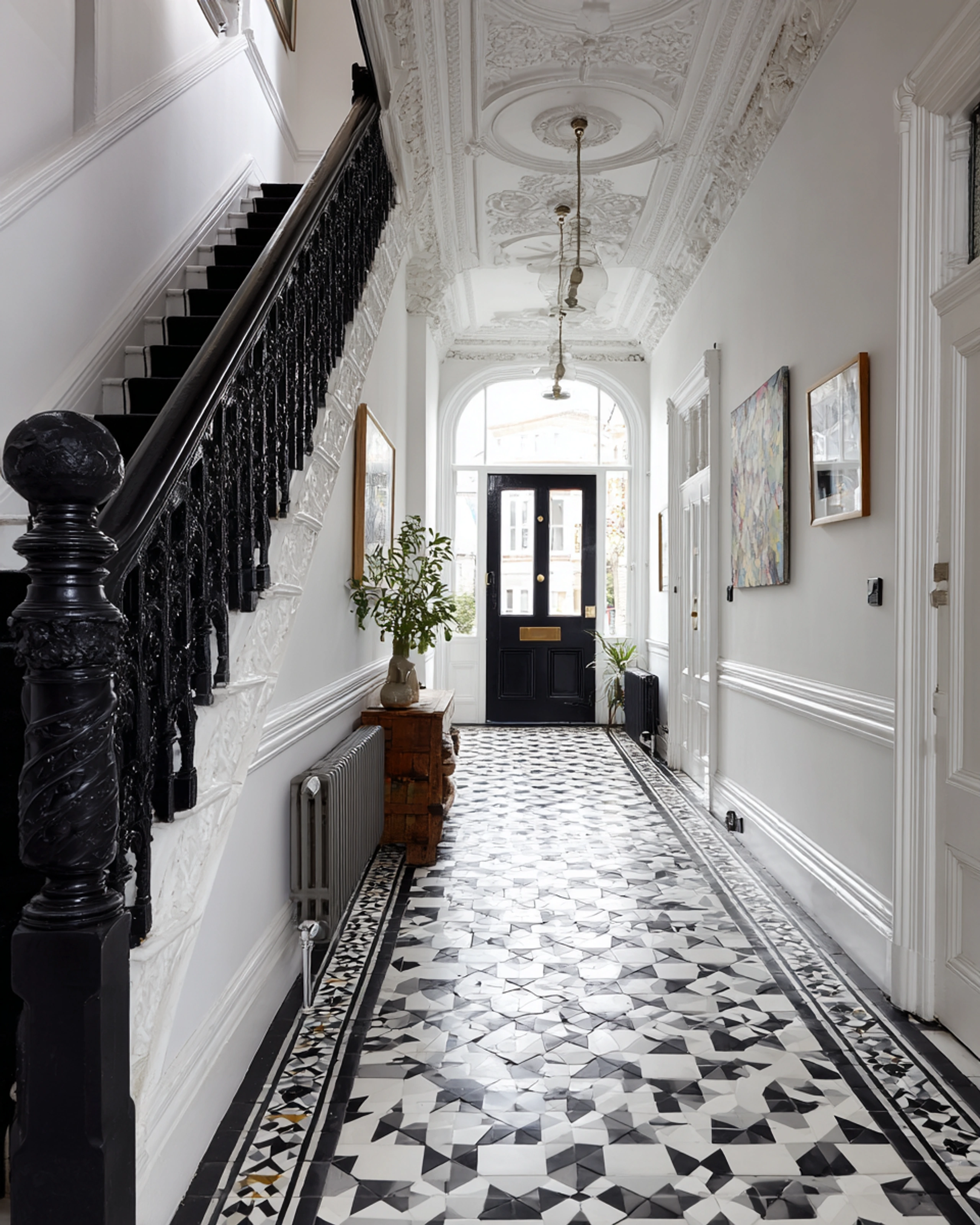 White period hallway with ornate plasterwork, a black staircase and geometric tiled floor
